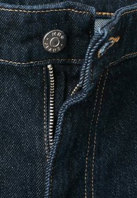 Gros plan d’un jean en denim bleu foncé avec une fermeture éclair argentée partiellement ouverte et un bouton en métal marqué "MNG JEANS."