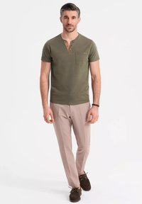 Camisa henley de manga corta en verde oliva con un bolsillo en el pecho, combinada con pantalones beige claro y zapatos de barco marrón oscuro. Diseño sencillo y casual.