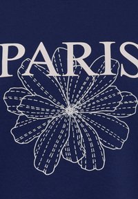 Marineblauwe T-shirt met "PARIJS" in grote witte letters, vergezeld van een wit bloemenpatroon dat gedetailleerde bloemblaadjes en stiknaden illustreert.