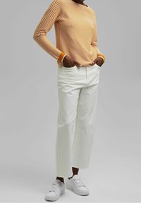 Gestreiftes langärmliges Hemd in Orange und Creme, kombiniert mit weißen schmal geschnittenen Hosen und weißen Sneakers. Einfaches Design, lässige Passform.