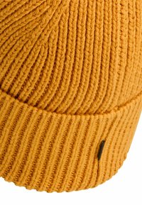 Orange strikket beanie med lodret ribbet mønster, en foldet kant og et lille sort mærke på siden. Blødt, struktureret uldstof.