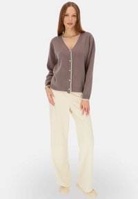 Sweter z dekoltem w serek, zapinany na guziki, w mauve z kontrastowym kremowym wykończeniem. Połączony z kremowymi spodniami o szerokich nogawkach i beżowymi butami. Gładka faktura.