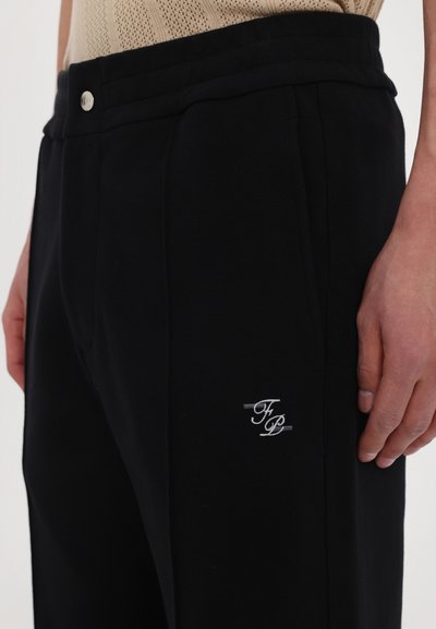 Black sweatpants made from soft material, featuring a logo embroidered in white on the left thigh and a drawstring waistband.