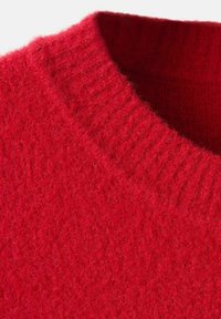 Primo piano di un caldo maglione rosso a maglia, che mostra il collo girocollo a coste e il morbido tessuto testurizzato.
