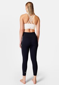 Leggings neri e un reggiseno sportivo bianco con spalline incrociate, realizzati in tessuto elasticizzato, progettati per attività fitness.
