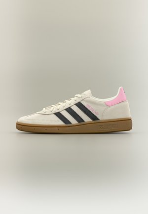 Λευκό αθλητικό παπούτσι Adidas με μαύρες ρίγες, ροζ ταβάνι φτέρνας, καουτσούκ σόλα και κείμενο "Spezial" στη πλευρά, εμφανιζόμενο από την εξωτερική πλευρά.