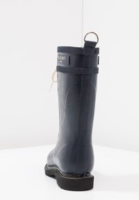 Botte de pluie en caoutchouc noire avec une finition texturée, une semelle robuste, une languette à l'arrière et un détail en lacet sur le côté.