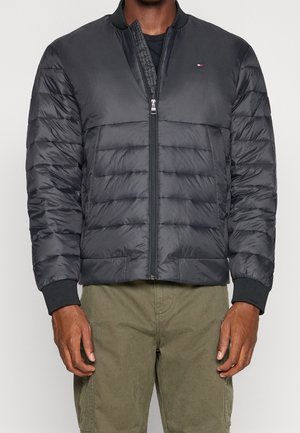 Man wearing black quilted bomber jacket with front zip and small logo on chest, paired with olive green cargo pants.