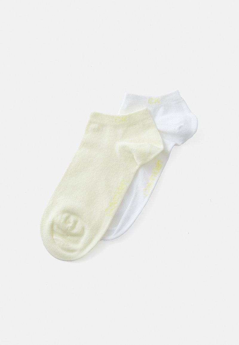 Två par ankelsockor: ett par ljusgula och ett par vita, båda gjorda av ribbad bomull med "CK"-logotyp tryckt i gult på sidorna.