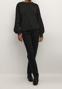 Zwarte trui met geribbelde mouwen en ronde hals, gecombineerd met zwarte slim-fit broek en zwarte enkellaarsjes met hak. Overal een gladde textuur.