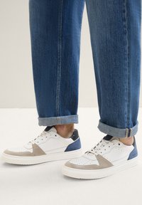 Weiße Ledersneaker mit beige und marineblauen Wildlederakzenten, perforierten Details und grauer Gummisohle. Kombiniert mit hochgekrempelten Denim-Jeans.