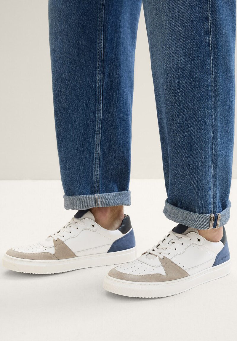 Weiße Ledersneaker mit beige und marineblauen Wildlederakzenten, perforierten Details und grauer Gummisohle. Kombiniert mit hochgekrempelten Denim-Jeans.