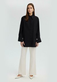 Black long-sleeve shirt with a collar and silver accents on the cuffs, paired with white flared pants and pointed-toe shoes.