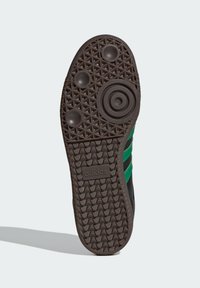Black sneaker outsole with green stripes, textured rubber sole, circular and raised grip patterns, and an embossed logo.