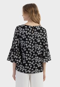 Blusa nera con motivo di margherite bianche, maniche svasate, scollatura rotonda e dettaglio a forma di chiave sul retro. Tessuto dalla superficie liscia.