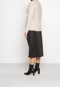 Lichtbeige trui, zwarte satijnen midi-rok, strakke enkellaarsjes. De trui heeft een losse pasvorm, de rok heeft een gladde textuur en de laarsjes hebben een gestroomlijnd ontwerp.