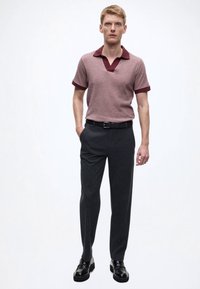 Piké med korte ermer i støvet rosa med mørkerød krage, kombinert med mørkegrå skreddersydde bukser og svarte skinnsko. Jevn tekstur og tettsittende design.