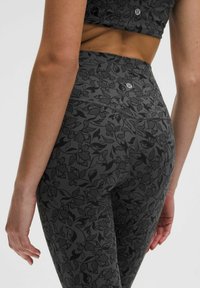Tamsiai pilkos aukšto juosmens legginsai su subtiliu gėlių raštu. Pagaminti iš elastingos medžiagos, juosmens juostoje yra logotipo detalė.