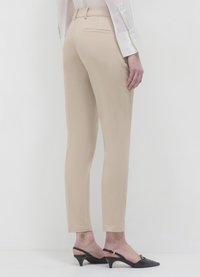 Pantalons beiges fuselés avec une texture lisse, dotés de poches arrière et d'une taille mi-haute. Associés à des mules à talons noires.