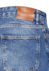 Poche arrière d'un jean en denim bleu avec des coutures orange et une étiquette en cuir marron portant l'inscription « 2Y PREMIUM » sur la ceinture.