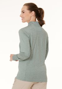 Langærmet pullover i lys grøn melange, med lynlås i halsen, netdetaljer på skuldrene og subtile sømadderinger på ryggen.