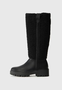 Botas negras con parte superior texturizada y suave, y parte inferior de cuero liso. Suela gruesa con un patrón de tracción robusto y detalle de cremallera lateral.