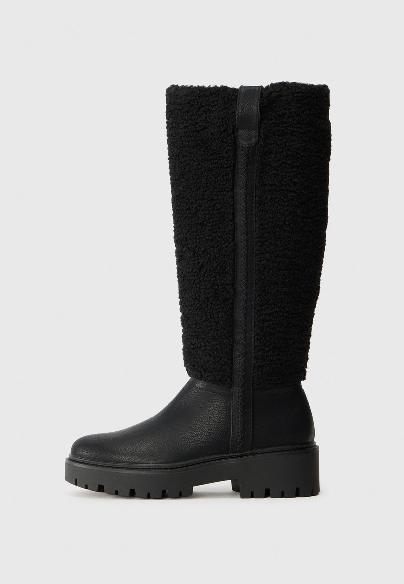 Botas negras con parte superior texturizada y suave, y parte inferior de cuero liso. Suela gruesa con un patrón de tracción robusto y detalle de cremallera lateral.