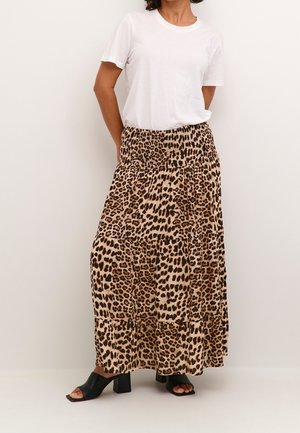 Woman wearing a white short-sleeve shirt, leopard print long skirt, and black heeled sandals standing against a plain background.