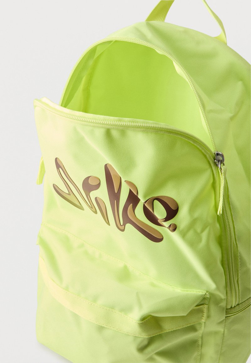 Mochila de color amarillo verdoso brillante con cremallera principal abierta y bolsillo frontal, con un gran logotipo estilizado de "Nike" en marrón en la parte delantera.