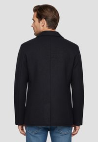 Manteau en laine bleu marine à coupe droite, col à cran et deux poches latérales. Texture lisse avec des détails de coutures subtiles au dos.