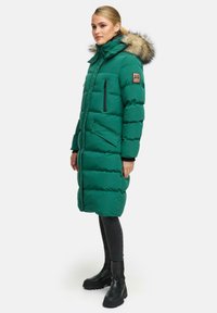 Zelena puhovka s kapuco obloženo z krznom, z zadrgo in snap žepi ter z ribastimi manšetami. Plašč je do kolen in ima kanalna prešita za izolacijo.