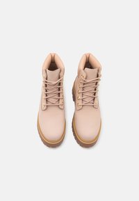 Botas de tobillo de cuero beige con punteras redondas, cuellos acolchados, ojales en tono dorado y suelas de goma texturizadas.