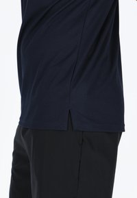 Camicetta blu navy a maniche corte realizzata in tessuto liscio, con uno spacco laterale e orlo dritto, abbinata a pantaloni neri.