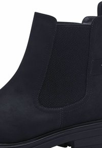 Svart mockalädersankelsko med en texturerad elastisk panel, slät yta, rund tå och en låg, stabil klack för stabilitet.