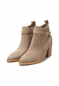Botas de tobillo de ante beige con punta afilada, patrón floral recortado, cremallera lateral y tacón de madera apilada. Correa ajustable con detalle de hebilla.