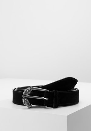 Ceinture en daim noir avec une boucle en métal argenté ornée de détails tissés en forme de feuille, enroulée sur une surface blanche sur un fond uni.