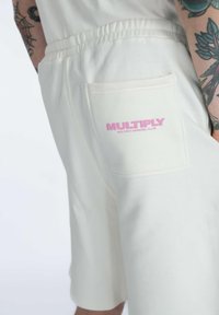 Kerman shorts made of cotton with an elastic waistband and a back pocket featuring pink "MULTIPLY" branding. Smooth texture, relaxed fit.