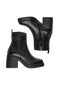 Un par de botas de cuero negro hasta el tobillo con tacones de bloque, cremalleras laterales y el logo "G-STAR" en el lado exterior de una de las botas.