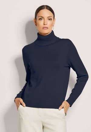 Dunkelblauer Rollkragenpullover aus weichem Strickstoff. Figurbetontes Design mit gerippten Ärmelbündchen und Saum, kombiniert mit hellen Hosen.