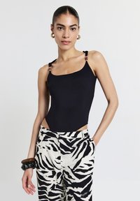 Body nero con scollo quadrato e spalline accentate. Abbinato a pantaloni bianchi con strisce zebrata nere. Materiale liscio con design aderente.
