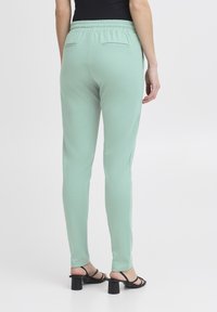 Mintgröna joggerbyxor med elastisk midja, två bakfickor och en mjuk textur. Kombineras med svarta klacksandaler.