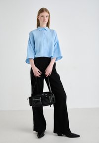 Camicia azzurra chiara, texture, con bottoni e maniche ampie, dotata di colletto. Abbinata a pantaloni neri a vita alta, a gamba larga, e una borsa nera.