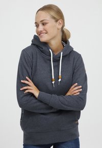 Sweat-shirt à capuche gris foncé avec des cordons blancs, des accents en bois et un tissu texturé. Il présente une coupe décontractée et des fentes sur les côtés.
