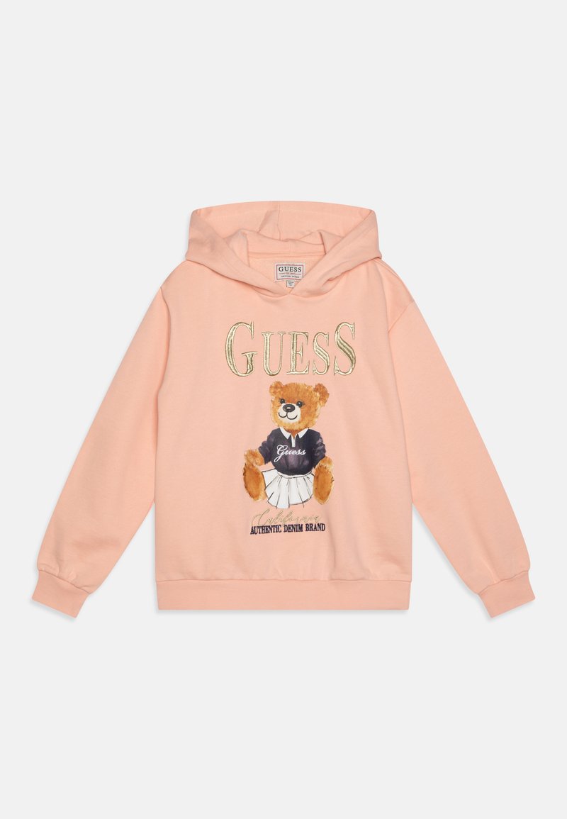 Ferskenfarget hettegenser med en grafikk av en bjørn i kjole med svart topp. "GUESS"-logo i gullbokstaver over illustrasjonen. Myk stoff.
