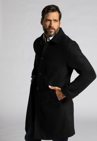 Abrigo de lana negro con cuello, botones de doble pecho y bolsillos laterales. Tiene mangas largas y un corte ajustado. Textura suave.