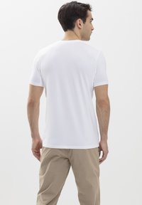 White short-sleeve t-shirt featuring a classic crew neckline, smooth texture, and a fitted shape, paired with beige trousers.