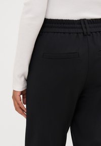 Sorte bukser med elastisk liv, med to baklommer, kombinert med en hvit, ribbet langermet topp. Glatt tekstur, uformell design.