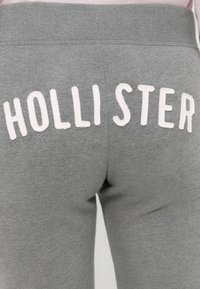 Γκρι φόρμα με απαλή υφή και ελαστική μέση, με το «HOLLISTER» κεντημένο με λευκά γράμματα στην πίσω πλευρά.