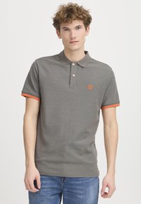 Grå polo skjorte med struktureret stof, to knapper ved kraven og orangerøde detaljer på ærmerne. Broderet logo på brystet.