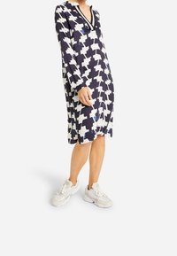 Šaty s dlouhým rukávem s námořnickým a bílým kostkovaným vzorem, s výstřihem do V, volným střihem, spárované se světle barevnými sportovními botami.